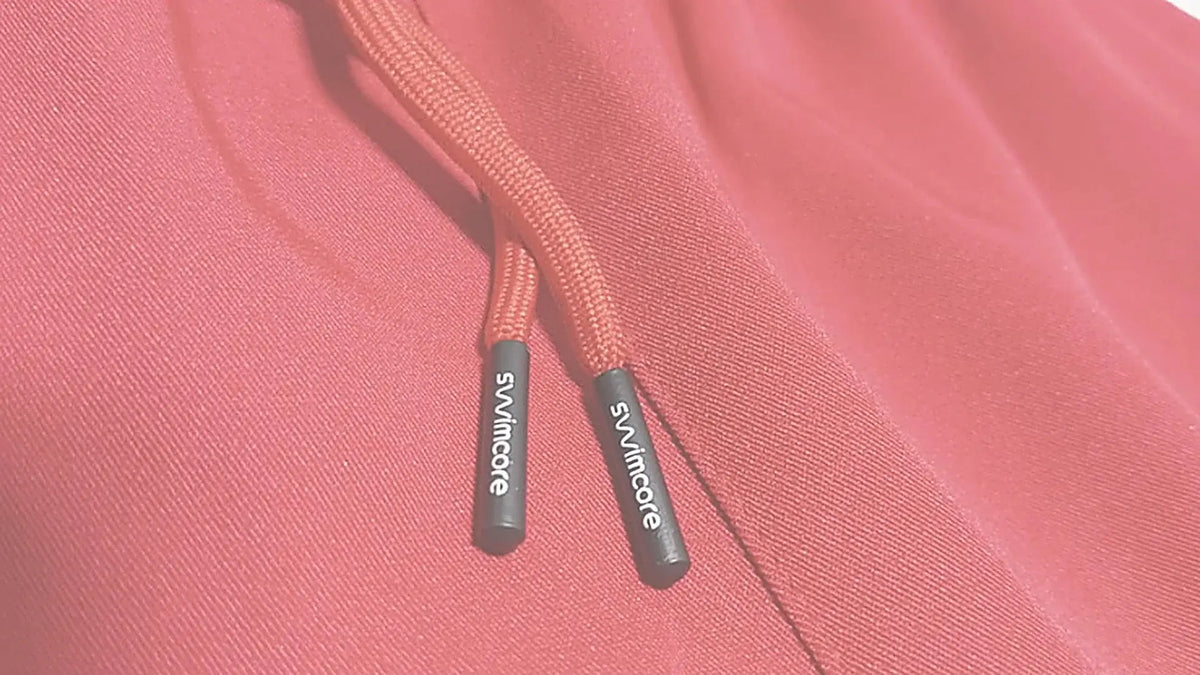 Close-up of the drawcord on Swimcore Academy red lifeguard shorts, with branded black cord tips