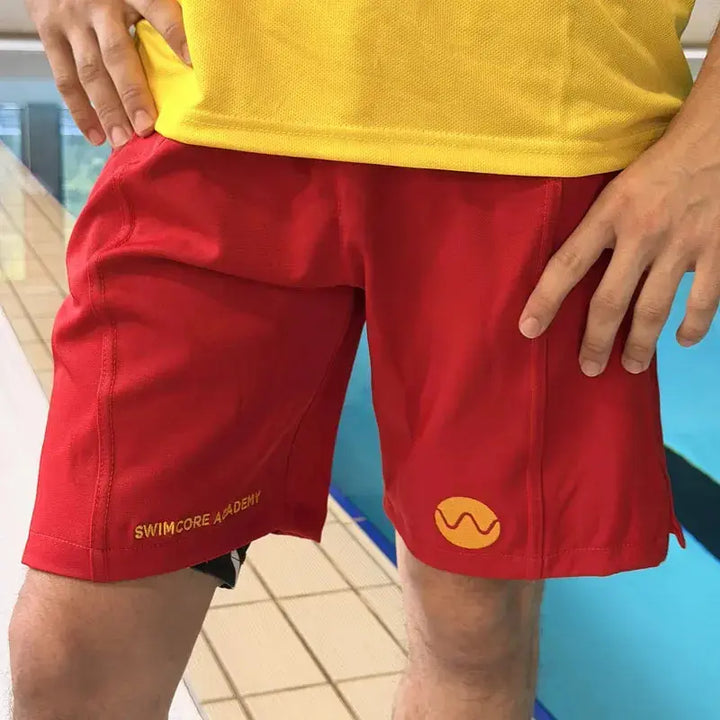 Red lifeguard shorts with yellow embroidered Swimcore Academy branding